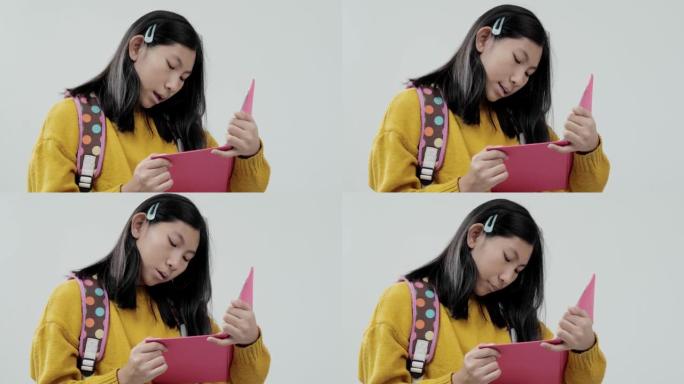 穿着黄色毛衣的亚洲女学生在灰色背景上阅读粉红色的书，生活方式的概念。