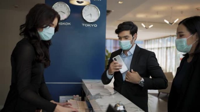 酒店柜台的商人和女商人以及接待员戴着医用口罩以防病毒。商务旅行中的商务人士在酒店办理入住手续