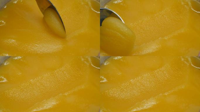 浓黄色蜂蜜收集在金属茶匙中。勺子在蜂蜜上留下了痕迹。特写。