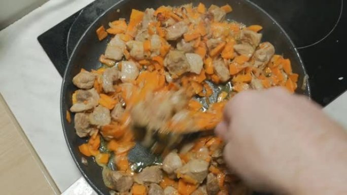 厨师在大锅中煎炸时，将烤猪肉与蔬菜混合。从顶部看。角度透镜。看起来很好吃。洋葱、胡萝卜和香料炒肉。4