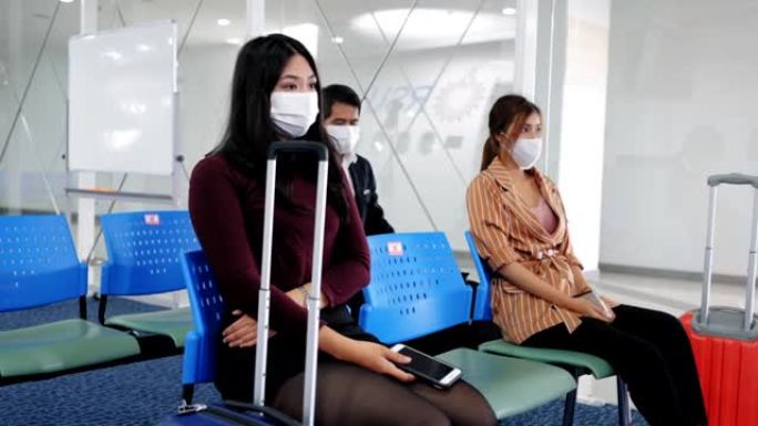 女航空乘客，旅行者，商人坐在社交距离上等待在柜台上排行，在航空公司柜台办理登机手续时交出护照。在登机