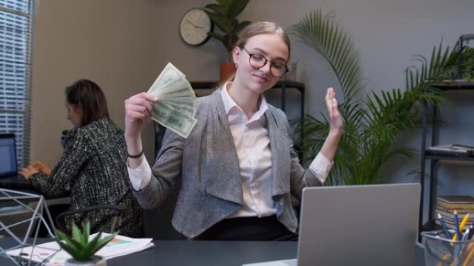 微笑的年轻女商人在办公室工作场所挥舞着一堆钱美元现金