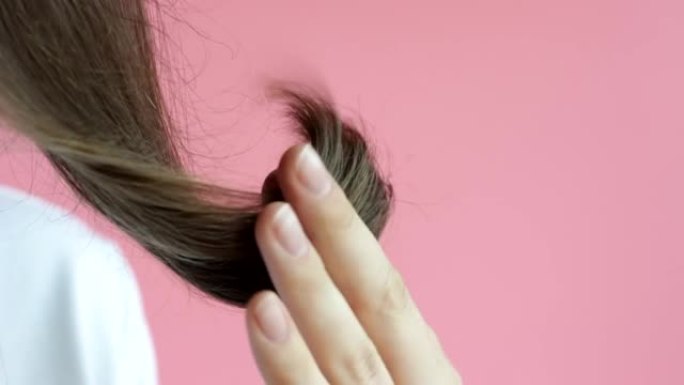 女孩手里拿着头发，两头分开，在粉红色背景上特写。