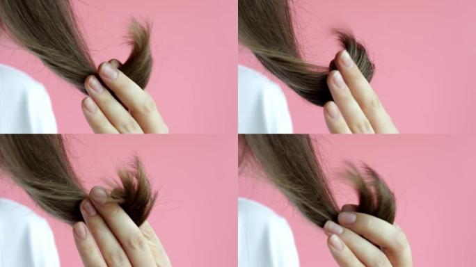 女孩手里拿着头发，两头分开，在粉红色背景上特写。