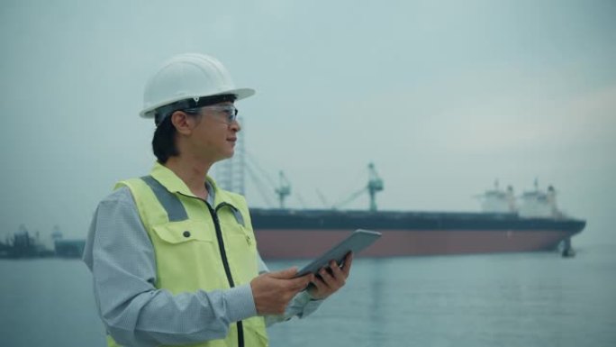 Asien男工程师在工业港口背景下使用未来派触摸屏。
