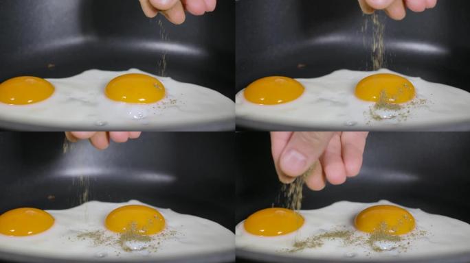 慢动作特写男人在煎锅上煮煎鸡蛋作为早餐，在家厨房。煎锅里的煎鸡蛋撒上磨碎的香料。手厨倒香料鸡蛋慢动作