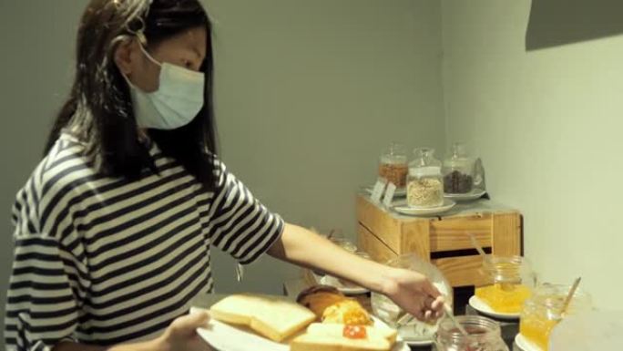 快乐的亚洲人戴着口罩，在酒店度假期间选择自助早餐，生活方式理念。