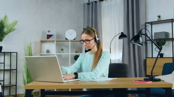 迷人的自信集中的20岁女孩戴着耳机坐在电脑前写大学或大学的家庭任务，慢动作