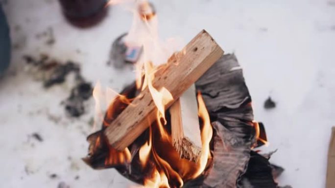 一名男子将手放在火上，火上的火堆在支撑火堆的雪块上燃烧。特写拍摄