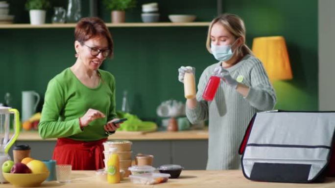 戴着口罩和手套的女性快递员为女性卸下生态食品