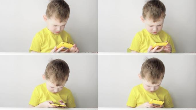 一个穿着黄色t恤的四岁男孩玩黄色智能手机。孩子和小玩意。