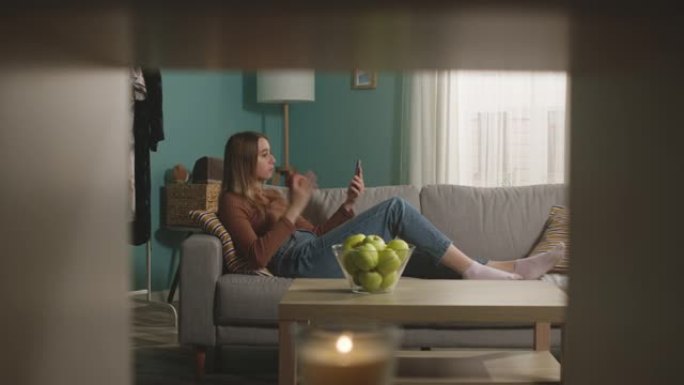 年轻女孩吃了一个红苹果，躺在沙发上，并通过视频链接讲话