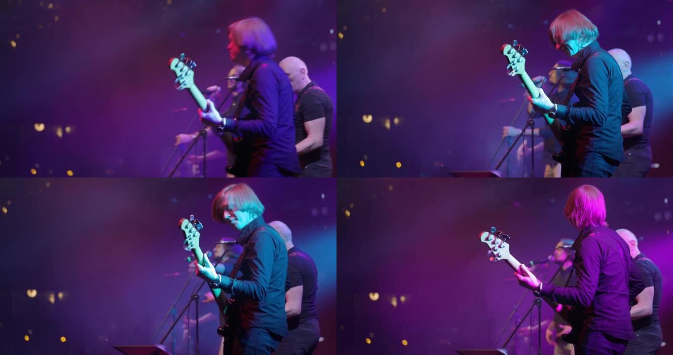 舞台上低音吉他手在音乐会上弹吉他的背面视图。慢动作