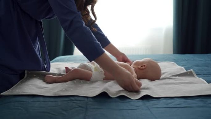 母亲用男婴做简单的运动，使婴儿骨骼和肌肉更强壮，新生儿躺在床上靠窗。