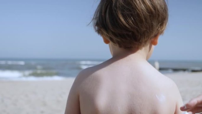 妈妈给孩子涂防晒霜。妈妈在海滩上给身体儿子涂防晒霜。母亲为孩子在海里洗澡做准备。海滩防晒快乐的家庭。