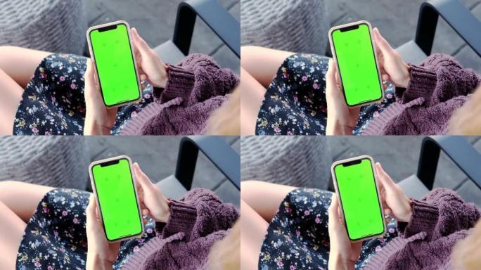空白数字智能手机在女性手中。女孩坐在椅子上，用绿屏模拟颜色键在手机上聊天，上网观看视频。
