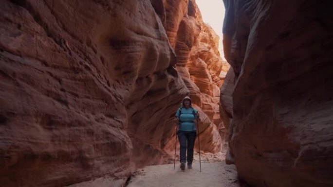徒步旅行者在带有橙色光滑岩石的深槽峡谷的干燥曲线河床上行走