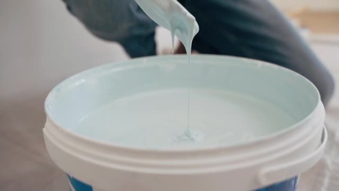男人的手用棍子搅动水桶里的油漆蓝色油漆滴入水桶家庭维修室修复施工特写