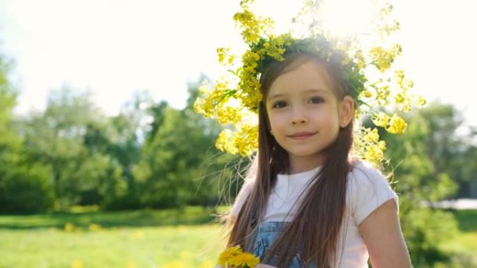 一个可爱的小女孩的肖像，头上戴着花环，手里拿着蒲公英，她在夕阳的背景下看着相机