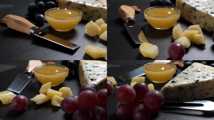 在页岩拼盘上切成薄片的奶酪，坚果，葡萄，蜂蜜和刀。旋转
