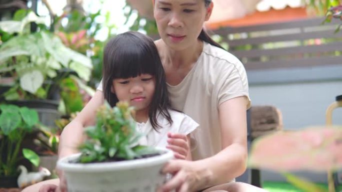 亚洲妇女和她的女儿一起享受时光，在家庭花园里种花。