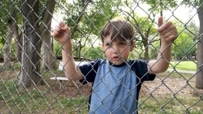 高加索人沉思的小男孩透过校园链条围栏摇晃它