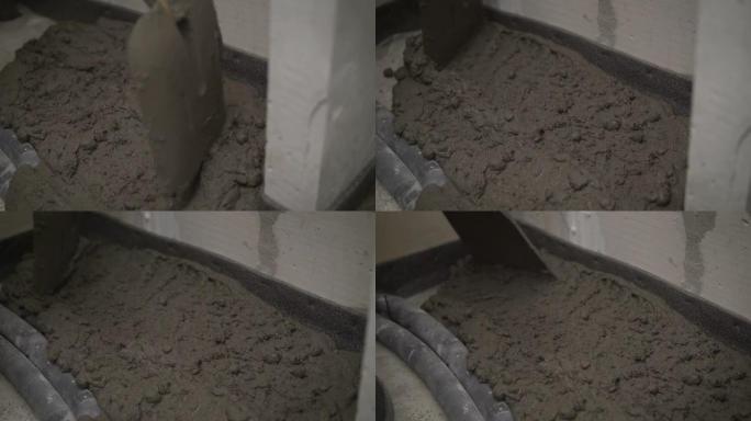 工人用铲子将溶液涂在水泥地面上。用混凝土砂浆填充地板。工人用抹刀对准。