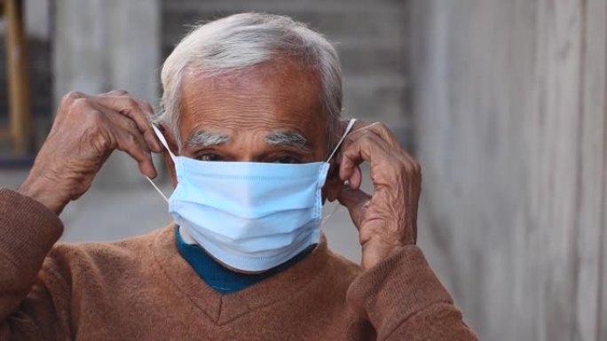 戴着面具挣扎的印度老人的肖像。坐在室内。在电晕病毒大流行2021年中老年人戴口罩的认识