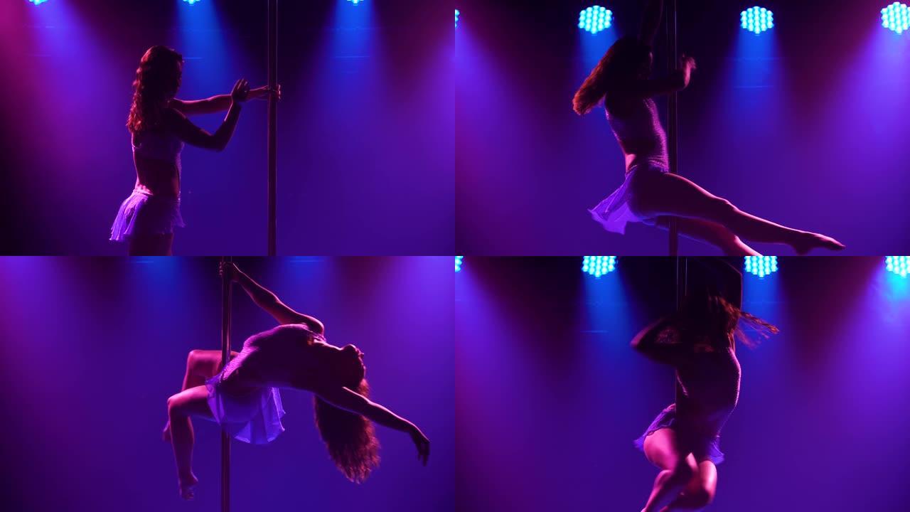 运动灵活的女人在一个黑暗的工作室里的一根杆子上旋转，里面有蓝紫色的霓虹灯。舞蹈飞行元素编舞，健美操，