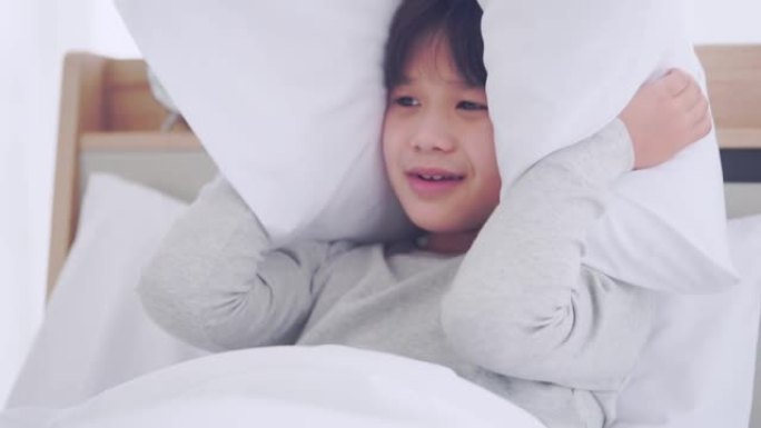 亚洲男孩正在用枕头遮住他的眼睛和耳朵，免受噪音和噩梦的恐惧。