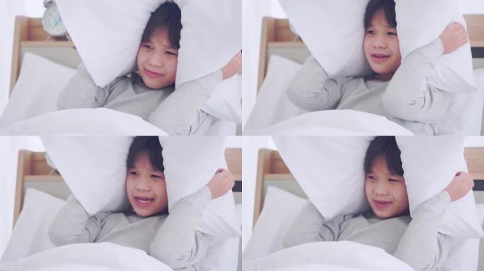 亚洲男孩正在用枕头遮住他的眼睛和耳朵，免受噪音和噩梦的恐惧。