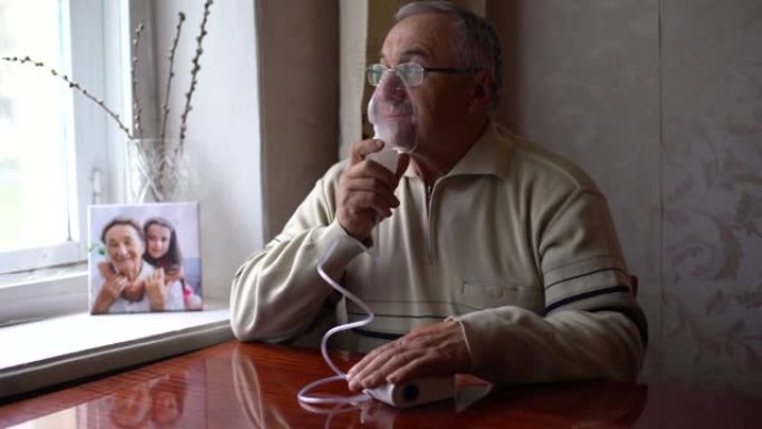 家里吸入流感的老人肖像。这位高个子白人在家里独自坐在沙发上，用喷雾器面罩吸入冠状病毒疾病。医疗保健概