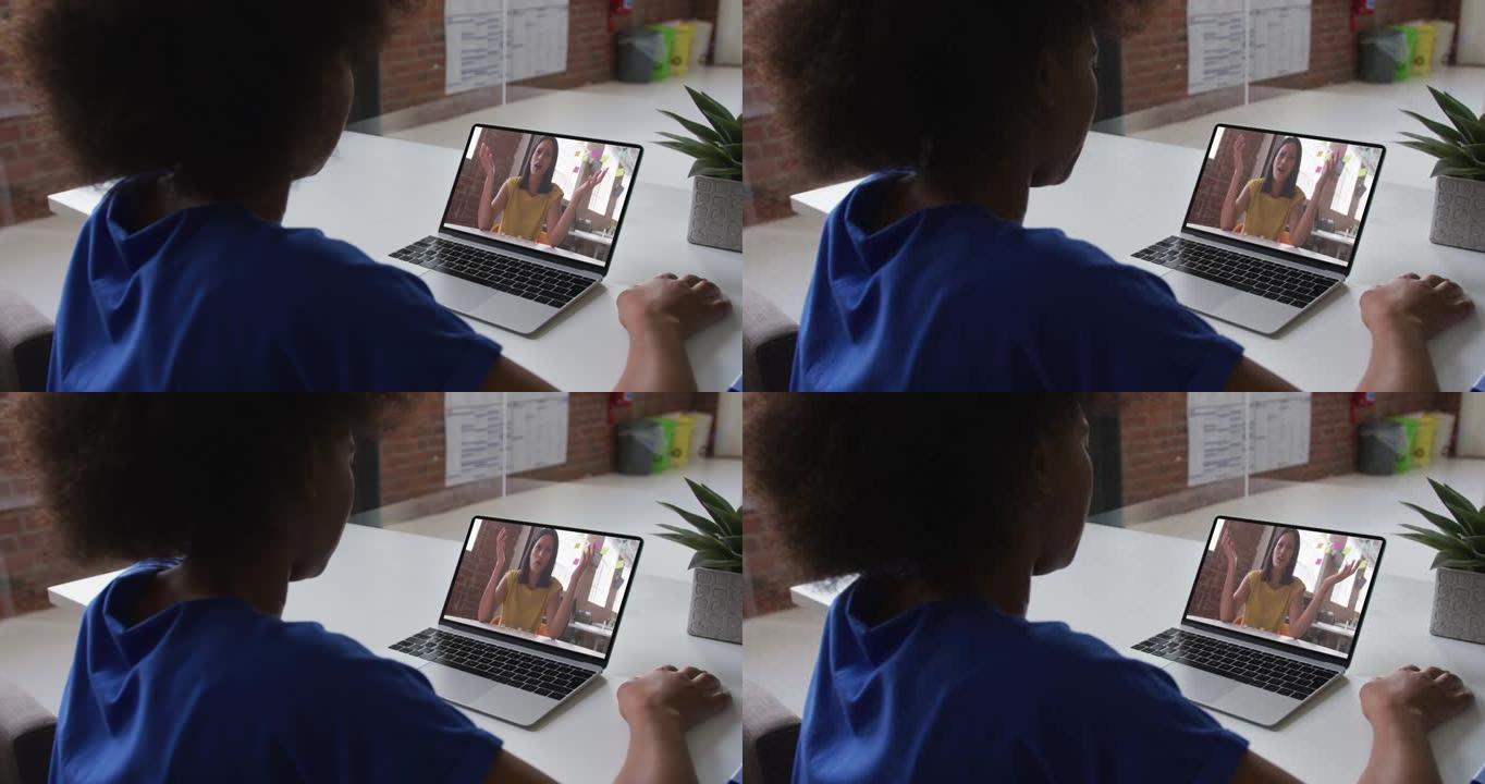非裔美国妇女在办公室与女同事在笔记本电脑上进行视频通话的后视图