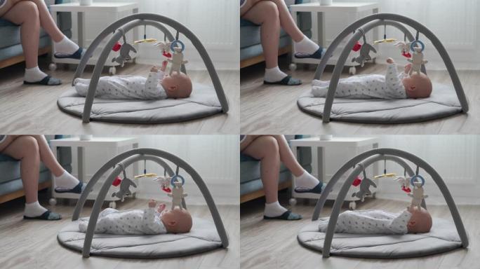 可爱的男婴躺在婴儿活动健身房游戏垫玩悬挂玩具，婴儿感官发育，2个月大的新生婴儿在客厅地板上