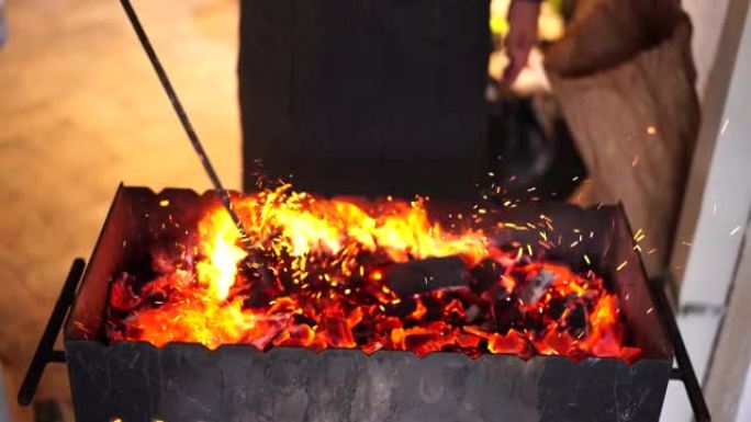 厨师正在火盆里搅拌燃烧的木炭。厨师点亮了烤架。