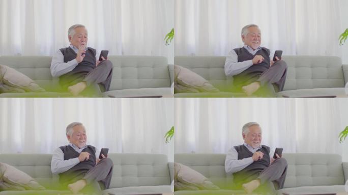 健康的幸福亚洲白发老人坐在沙发上使用手机VDO会议在线与家人见面并在家里微笑，居家生活方式的理念
