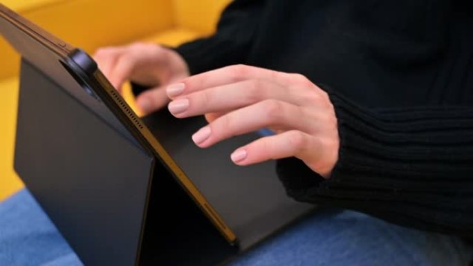 年轻的内容创作者在黄色沙发上使用她的平板电脑。舒适的在家工作环境。关闭打字