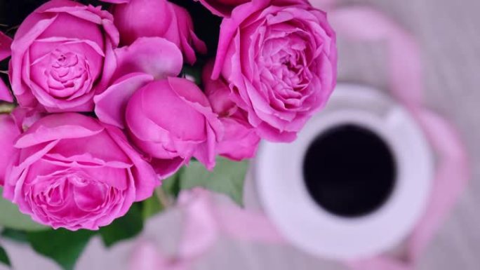 一杯咖啡和粉红玫瑰。假日概念，生日的玫瑰花花束，早餐的花束。女人喝卡布奇诺