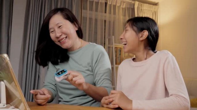 亚洲女孩帮助她的母亲检查健康设备，并在新型冠状病毒肺炎，保健和检疫生活方式概念的夜晚在家中餐桌上的数
