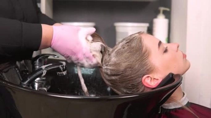 美发师在洗脸盆中客户的湿头发上泡沫洗发水。