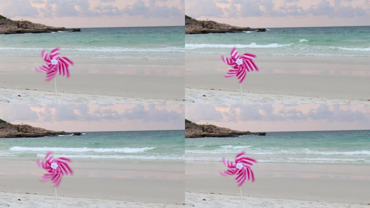 粉红风车玩具在白色沙滩上旋转，五颜六色的风力发电机 (风车) 在沙滩上，夏天的大海和蓝天为背景。