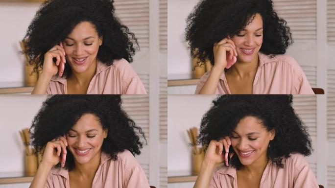 可爱的非洲裔美国女人在手机上聊天，微笑着开心。黑色黑发女人，卷发，坐在明亮的房间里摆姿势。特写。慢动