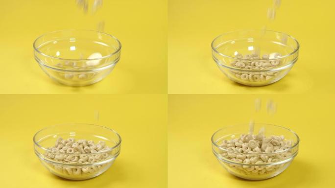 营养丰富的燕麦片圆形薄片落在黄色背景上的透明早餐碗中，与世隔绝。