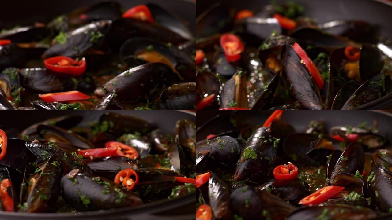 在平底锅中关闭煮熟的香贻贝。贻贝和辣椒片在黑锅中旋转