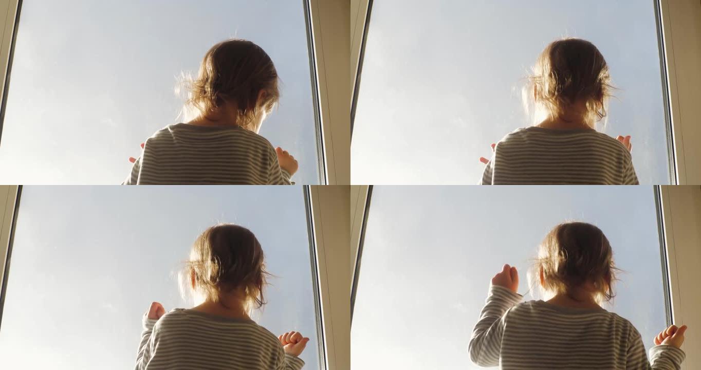 小孩子正站在窗户上，看着夕阳下的蓝天，用手敲窗户玻璃寻找出口