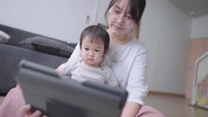 愉快的妈妈和聪明的婴儿在平板电脑上观看在线教育孩子频道，年轻的成年妈妈教女儿回答一个问题，可爱的女婴