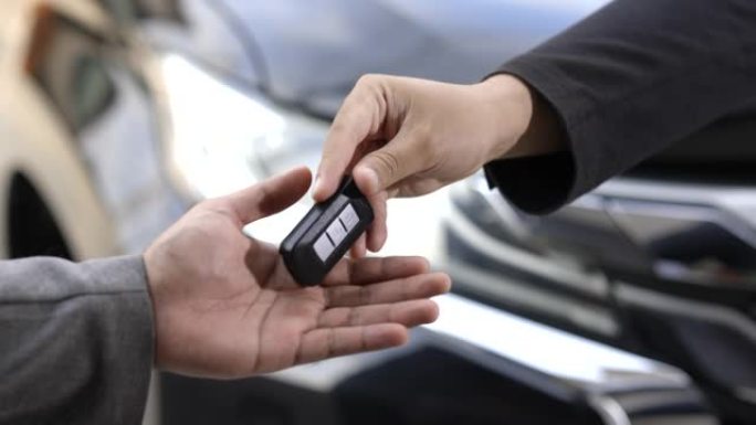 关闭商人，他的手展示或给汽车钥匙，以供客户购买新车。买卖租车概念。