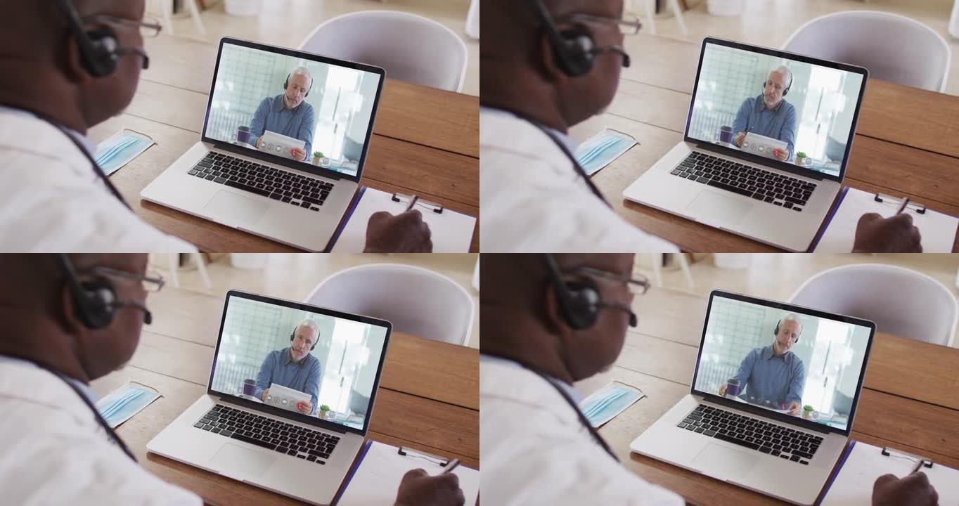 非裔美国男性医生戴着电话耳机在笔记本电脑上进行视频通话时做笔记