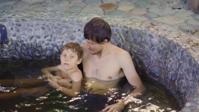 年轻人和他的儿子在装满草药输液的石头浴中放松。草药概念