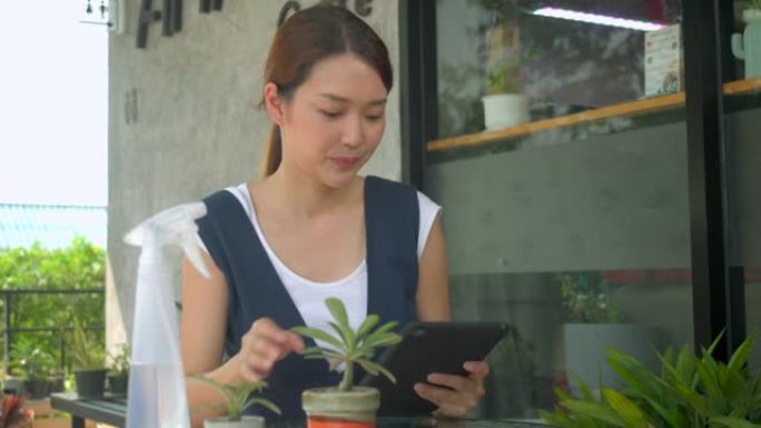 开朗的亚洲女性植物和持有使用平板电脑拍摄花园中生长的有机观赏植物的照片，以进行社交上传。爱好、生活方